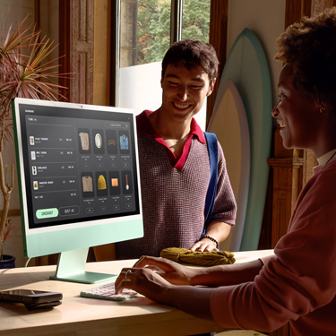 Um funcionário atrás do balcão de uma loja de pranchas de surfe usa um iMac para concluir uma compra para um cliente.