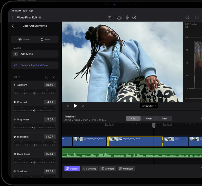 iPad Pro, front exterior, black display bezel, display showing video editing app with a picture of a model in a blue coat and black and white printed pants, colour adjustment panel open on the left with various video effects and sliders, timeline at the bottom with multiple video clips and audio tracks