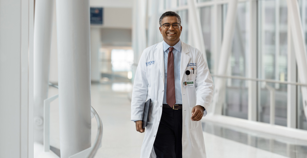 طبيب يحمل جهاز MacBook تحت ذراعه اليمنى أثناء المشي.