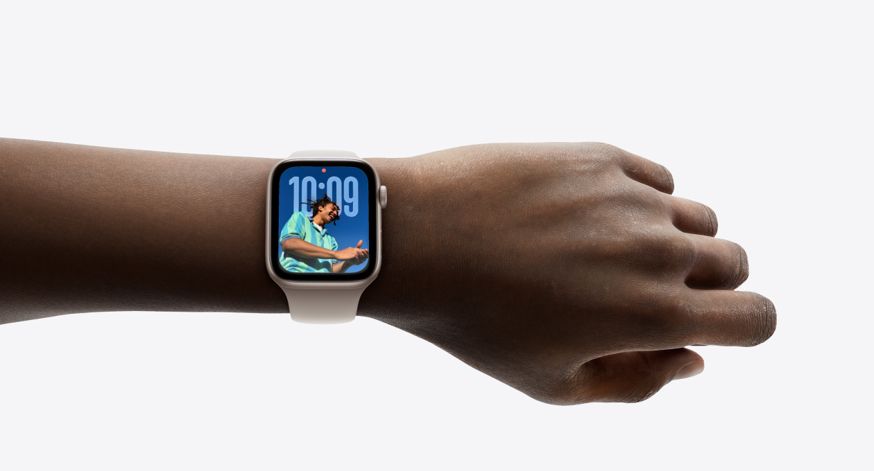 Close-up of Apple Watch in Rose Gold with rubber strap on a person’s wrist, showing Time app in new Liquid Glass design