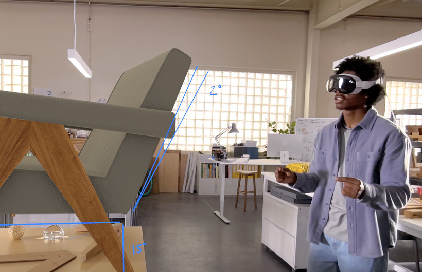 Eine Person mit einer Apple Vision Pro misst mit Handbewegungen eine 3D Projektion eines Stuhls