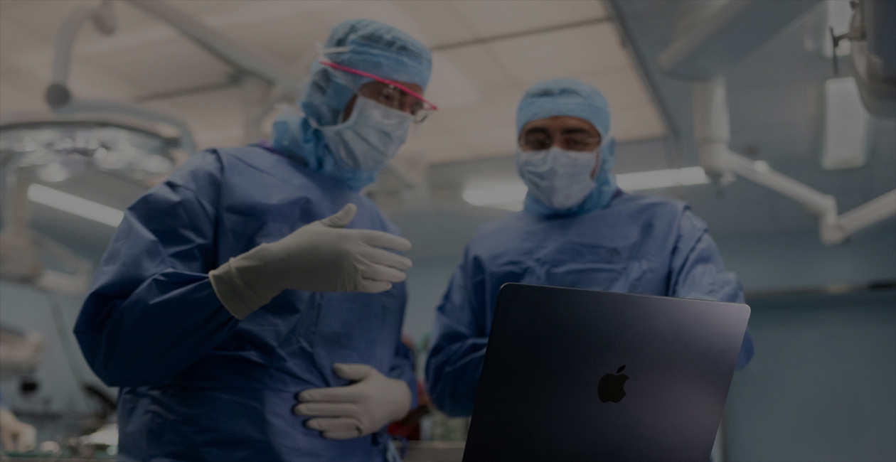 Two surgeons in scrubs looking at a MacBook Pro in the operating theatre.
