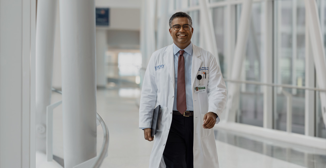 Médico segurando o MacBook sob o braço direito enquanto caminha.