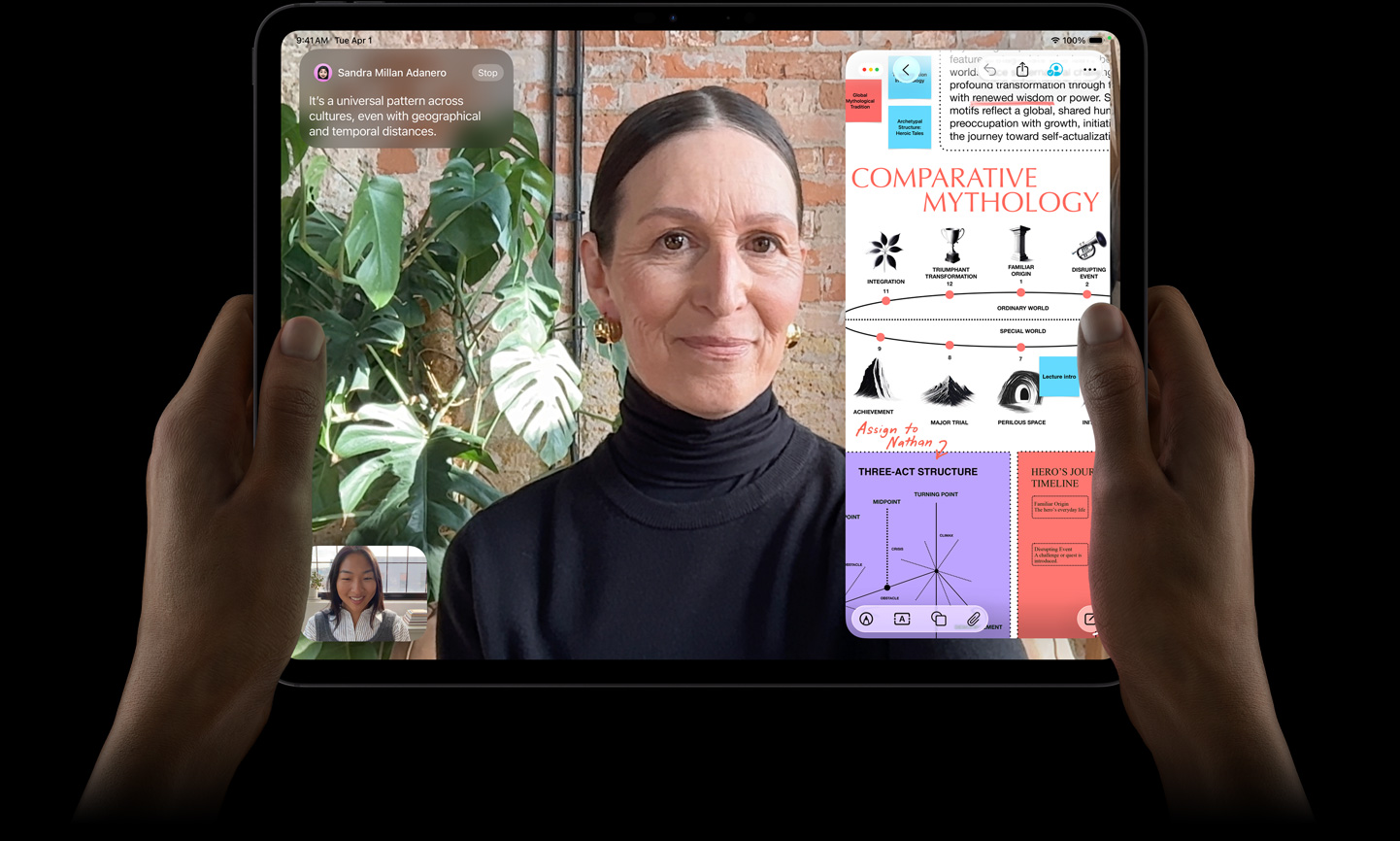 iPad Pro, esikülg, kosmosemust värv, mõlemad käed hoidmas seda horisontaalpaigutuses, ekraani must serv, ümarad nurgad, ekraanil tõlgitakse reaalajas FaceTime’i vestlust ning haridusrakendus näitab esitlust “Võrdlev mütoloogia” teksti, diagrammide ja käsitsi kirjutatud märkmetega