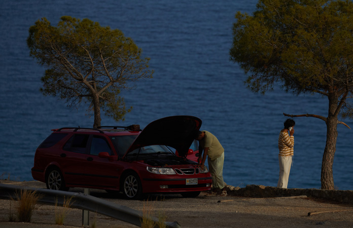 A car stranded by the side of a road with two people standing nearby