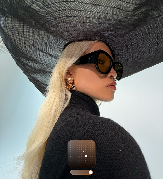 Portret al unei femei ce poartă o pălărie neagră cu boruri largi, demonstrând stilul fotografic Luminos, care luminează fotografiile realizate în condiții de lumină scăzută sau în Modul Noapte.