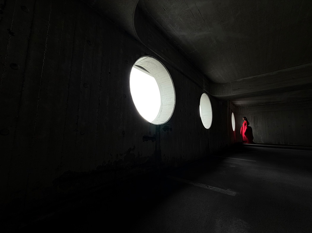 O femeie îmbrăcată într-o rochie roșie stă să fie fotografiată într-o cameră goală. Aplicația Poze comută între următoarele distanțe focale pentru a demonstra capabilitățile sistemului de camere pro: 200 mm, 100 mm, 48 mm, 35 mm, 28 mm, 13 mm și macro