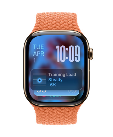 Apple Watch i roséguld med ett flätat armband i mandarin. Urtavlan visar ett datum längst upp till vänster, klockslaget med siffror längst upp till höger, widgeten Träningsbelastning längst ner, allt i halvgenomskinligt Liquid Glass.
