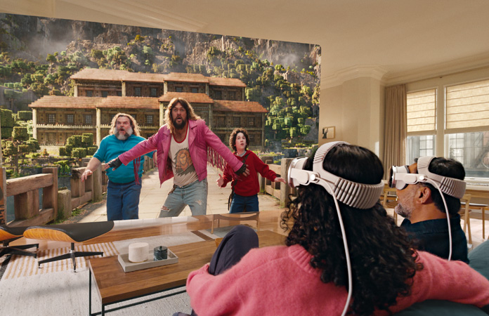 Deux personnes assises côte à côte sur un canapé, portant un Apple Vision Pro et regardant Minecraft, le film, sur un écran qui s’étend d’un bout à l’autre de la pièce