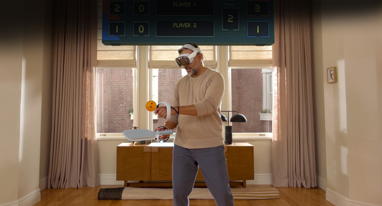Un homme portant un Apple Vision Pro et tenant des manettes Playstation VR2 Sense de Sony jouant à Pickle Pro, un tableau de pointage spatial au-dessus de la tête