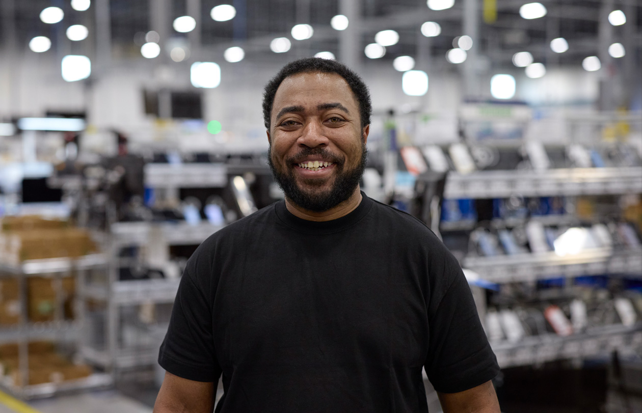 An employee stands in a logistics and repair center, smiling at the camera